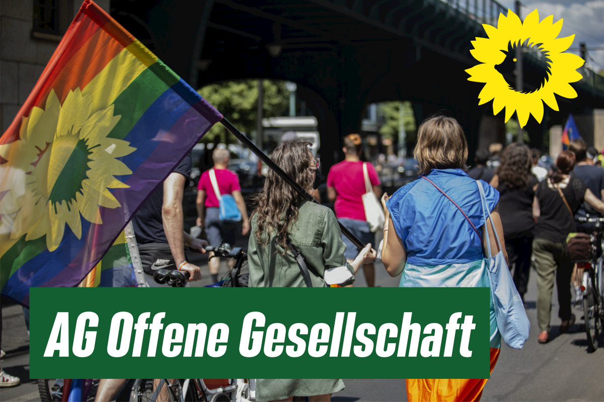 Auf einer Demonstration wird eine Regenbogen-Fahne mit der bündnisgrünen Sonnenblume darauf getragen. Text im Bild "AG Offene Gesellschaft".