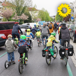 Eine größere Gruppe von Kindern und Erwachsenen fährt eine Wohnstraße entlang, viele tragen Helme und Warnwesten. Es sind geparkte Autos am Rand der Straße zu sehen und Bäume mit Blüten und jungen Blättern. In der oberen rechten Bildecke erscheint der Sonnenigel als Logo von B'90/Grüne in Berlin.