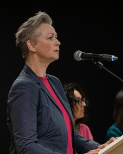 Eine Frau mit kurzen Haaren steht an einem Mikrofon und spricht. Es ist die Pankower Bürgermeisterin Cordelia Koch. Sie trägt ein dunkles Sakko und ein pinkes Oberteil. Im Hintergrund sitzen weitere Personen auf der Bühne.